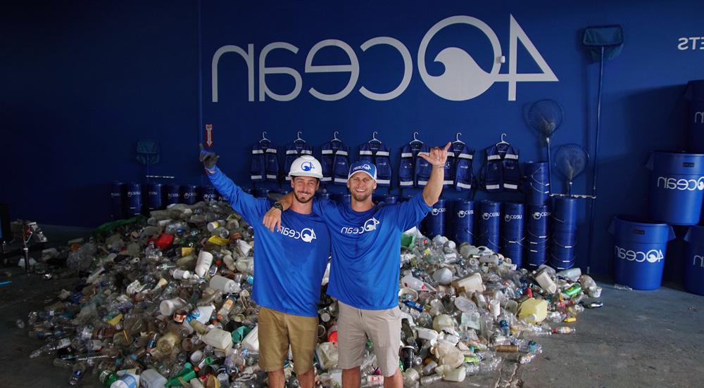 两个男人站在一个仓库的垃圾堆里，衬衫上写着4Ocean，墙上的背景是4Ocean的标志.